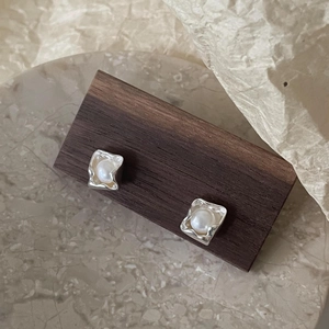 Detailed macro view of silver irregular frame pearl earrings on a wooden display stand