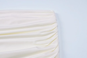 Dettaglio del tessuto increspato bianco crema con eleganti pieghe sulla superficie dell'abito