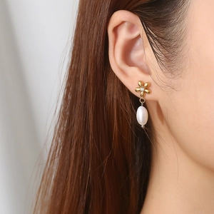 Close-up of gold flower pearl drop earrings with zircon studs worn by a model