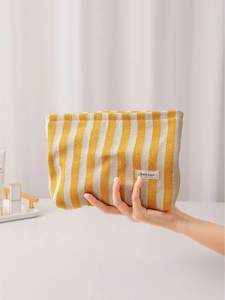 Minimalist striped canvas cosmetic bag in yellow and beige colors held by hand