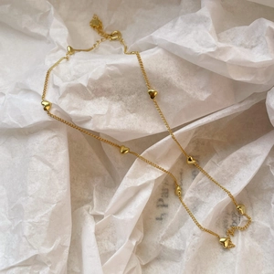 Macro shot of gold heart necklace with multiple charms on white textured background