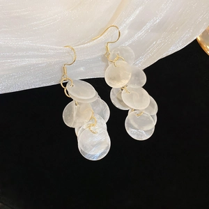 Close-up of scallop sequin tassel earrings on white silk fabric with elegant lighting