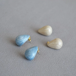 Macro view of teardrop enamel earrings with marble texture and gold plating