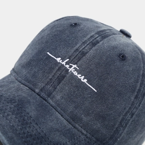 Close-up of white script embroidery on vintage washed dark gray cotton baseball cap