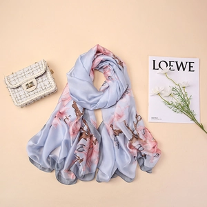 Detail of silk satin scarf with pink magnolia floral prints on a light blue fabric surface