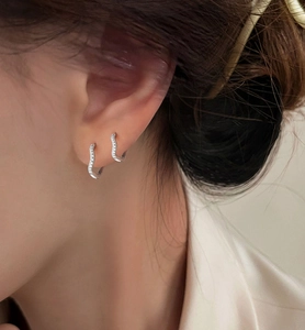 Close-up of silver-tone wave curve earrings with pavé set zircon stones on ear
