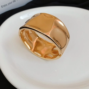 Close-up of golden wide cuff bracelet with irregular ripple texture on white ceramic plate