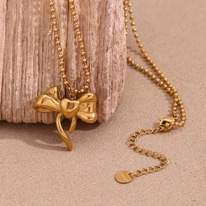 Close-up of a 18K gold plated stainless steel bow and heart pendant on a wooden stand