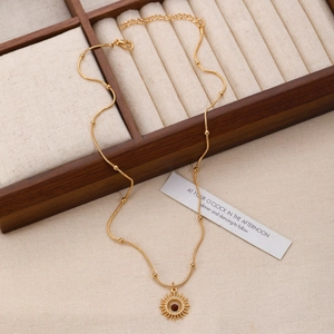 Detailed macro of vintage sunburst pendant with red gemstone on golden beaded chain necklace