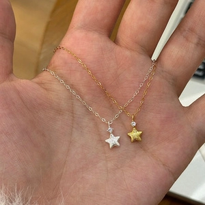 Detailed view of silver and gold star pendants with zircon held in hand