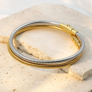 Detail of two-tone gold and silver snake chain bracelet on a stone pedestal