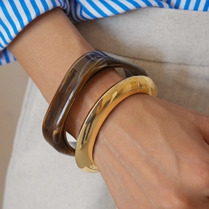 Detail of gold metal and dark brown resin bangle set worn on a model's wrist