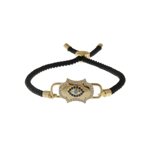 Adjustable gold Evil Eye bracelet with blue crystals and black braided rope on white background