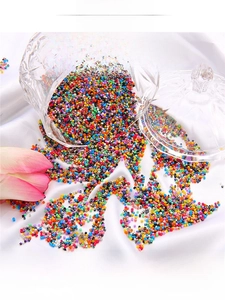Macro shot of 2mm colored glass seed beads scattered on white silk for DIY jewelry making