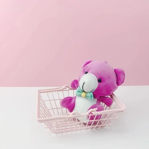 Plush teddy bear with teal bowtie inside a pink metal wire desktop storage basket