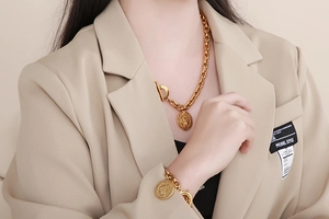 Close-up of model wearing chunky gold chain necklace and bracelet set with coin pendants