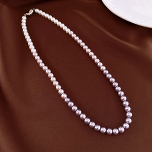 Detail of gradient pearl necklace with silver clasp on a brown silk background
