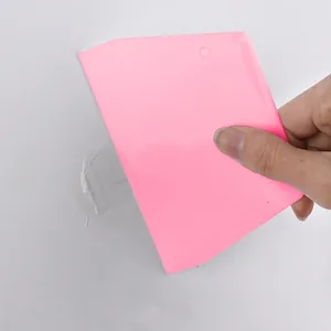 Pink plastic putty scraper tool being used to apply filler on a white wall surface