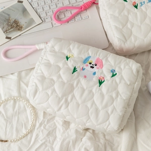 Detail of heart-quilted texture and colorful puppy embroidery on a white makeup bag