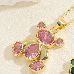 Detailed view of a golden bear pendant with pink zircon teardrop stones on a white surface
