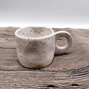 Minimalist ceramic mug with black ink splatter pattern and thick ring handle on wooden desk