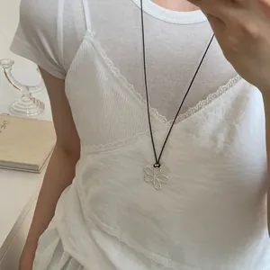 Dettaglio di un ciondolo a fiore in argento su un cordino nero indossato da una modella