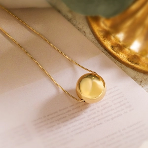 Minimalist 18K gold plated bead pendant necklace with fine chain on a decorative background