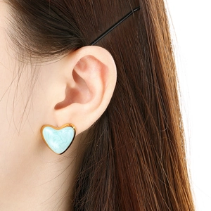 Close-up of a model wearing a light blue heart-shaped enamel earring with gold trim detail