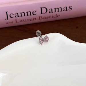 Macro detail of silver bow earring with pink heart zircon on a white ceramic dish