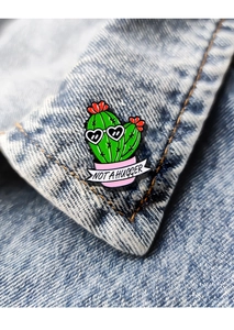 Detail of cute cactus enamel pin with 'NOT A HUGGER' text on blue denim fabric