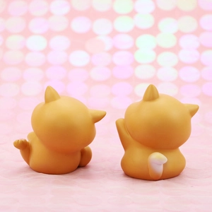 Close-up of two cute orange resin lucky cat figurines with soft pink bokeh background