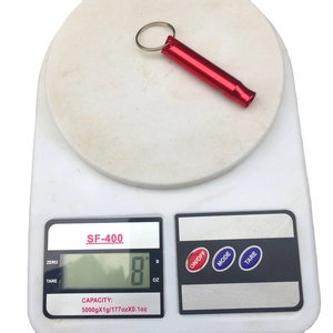 Aluminum emergency whistle in red finish with key ring on a digital scale weighing 8g