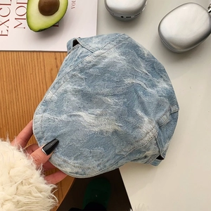 Flat lay of retro washed denim beret with embroidery next to silver headphones and fruit