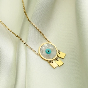 Gold evil eye pendant necklace with tassels on light green silk background
