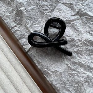 Macro-detail van een zwarte glanzende haarclip in de vorm van een strik op grijze basis