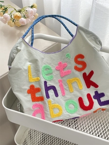 Detail of chenille embroidery lettering and woven handles on a canvas tote bag