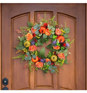 Detail of autumn wreath with orange roses and pumpkins on a rustic brown wooden door