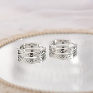 Close-up of silver textured hoop earrings with carved patterns on a reflective mirror