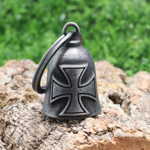Close-up of vintage iron cross biker bell on a rustic bark surface with grass backdrop