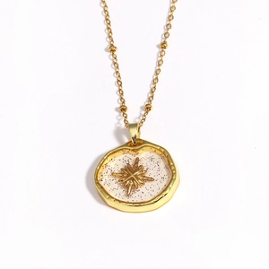 Detail of gold necklace with star and purple resin charms on white background