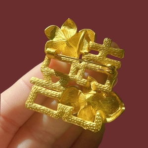 Macro shot of matte gold Xi character brooch with floral relief and brushed metal texture