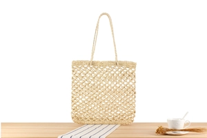 Detail of hand-woven hollow mesh beige tote bag with long handles on a wooden table