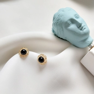 Macro detail of retro round gold stud earrings with black onyx on a textured white base