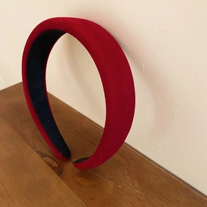 Side view of a vintage red velvet padded headband against a wall with soft shadows
