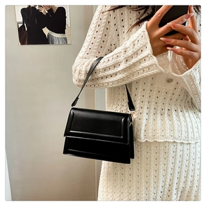 Detail shot of a stylish black leather handbag held by a model in a white knit outfit
