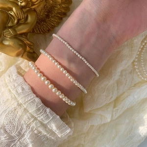 Detailed view of layered white pearl bracelets in three sizes on a delicate lace background