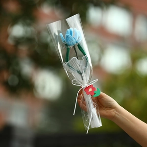 Handmade blue tulip plush bouquet with white ribbon and red gift tag in outdoor setting