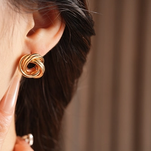 Gros plan de boucles d'oreilles nœuds dorés portées par un mannequin au style épuré