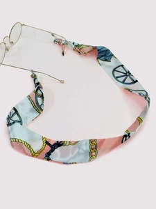 Close-up of golden round frame glasses with a vintage silk ribbon chain on pink surface