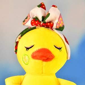 Close-up of cute yellow plush duck with strawberry bow headband and lemon cheek embroidery.